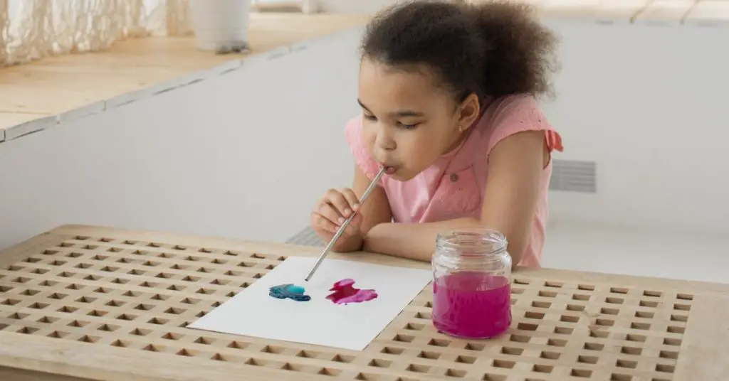 Child blowing paint with straw